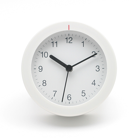 無印良品 アナログ目覚まし時計。マットな質感のホワイト筐体に、視認性を極めた黒のサンセリフ体数字を配置。円形ベゼルの上部に施された赤いインジケーターが、回転操作による直感的なアラーム設定機能を示唆するミニマルなデザイン。