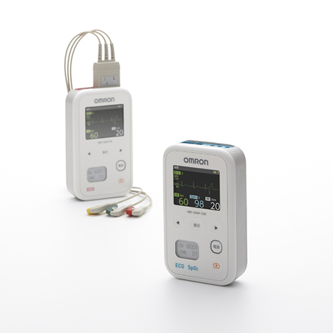 オムロン ヘルスケア株式会社 心電送信機「HBP-2030P」のプロダクトデザイン。白い丸みを帯びた縦長の筐体に、心電図波形や数値を表示するカラー液晶画面と操作ボタンが配置され、上部に電極ケーブルを接続した医療機器。