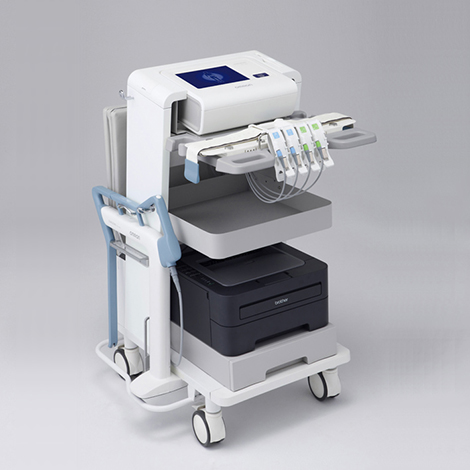 オムロンヘルスケア株式会社 医療用内臓脂肪測定装置「HDS-2000 DUALSCAN」のプロダクト。白い筐体の測定ユニット、グレーのトレイ、下部の黒いプリンターが4輪キャスター付きの白いフレームに垂直に配置されている。側面にはプローブが収められている。