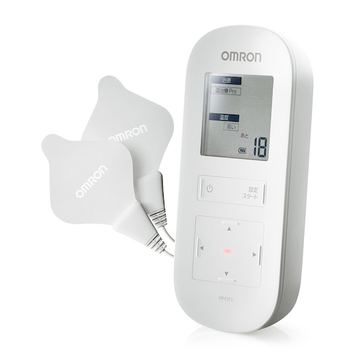 オムロンヘルスケア株式会社 温熱低周波治療器「HV-F311」のプロダクトデザイン。白を基調とした角に丸みのある縦長の筐体。上部に液晶画面、中央に電源・設定ボタン、下部に十字ボタンが配置され、左側にはコードで繋がった2枚のグレーのパッドがある。